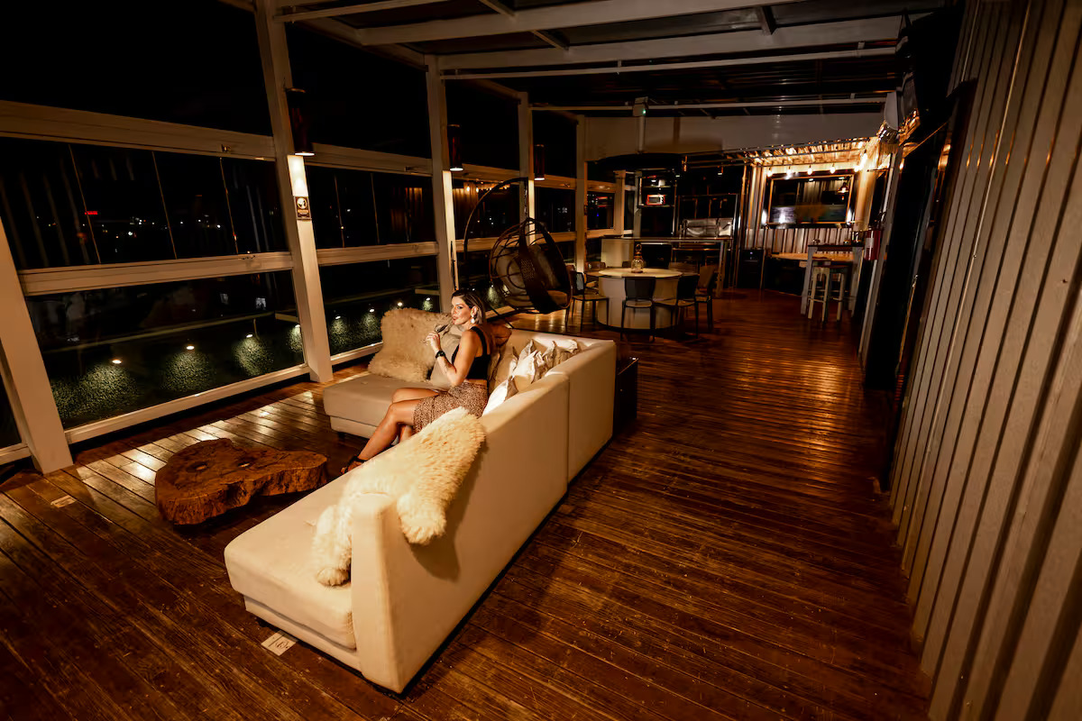 Deck noturno iluminado de cobertura mobiliada em Curitiba, com sofás e estrutura de madeira, ideal para quem procura uma cobertura no Rebouças com charme e praticidade.
